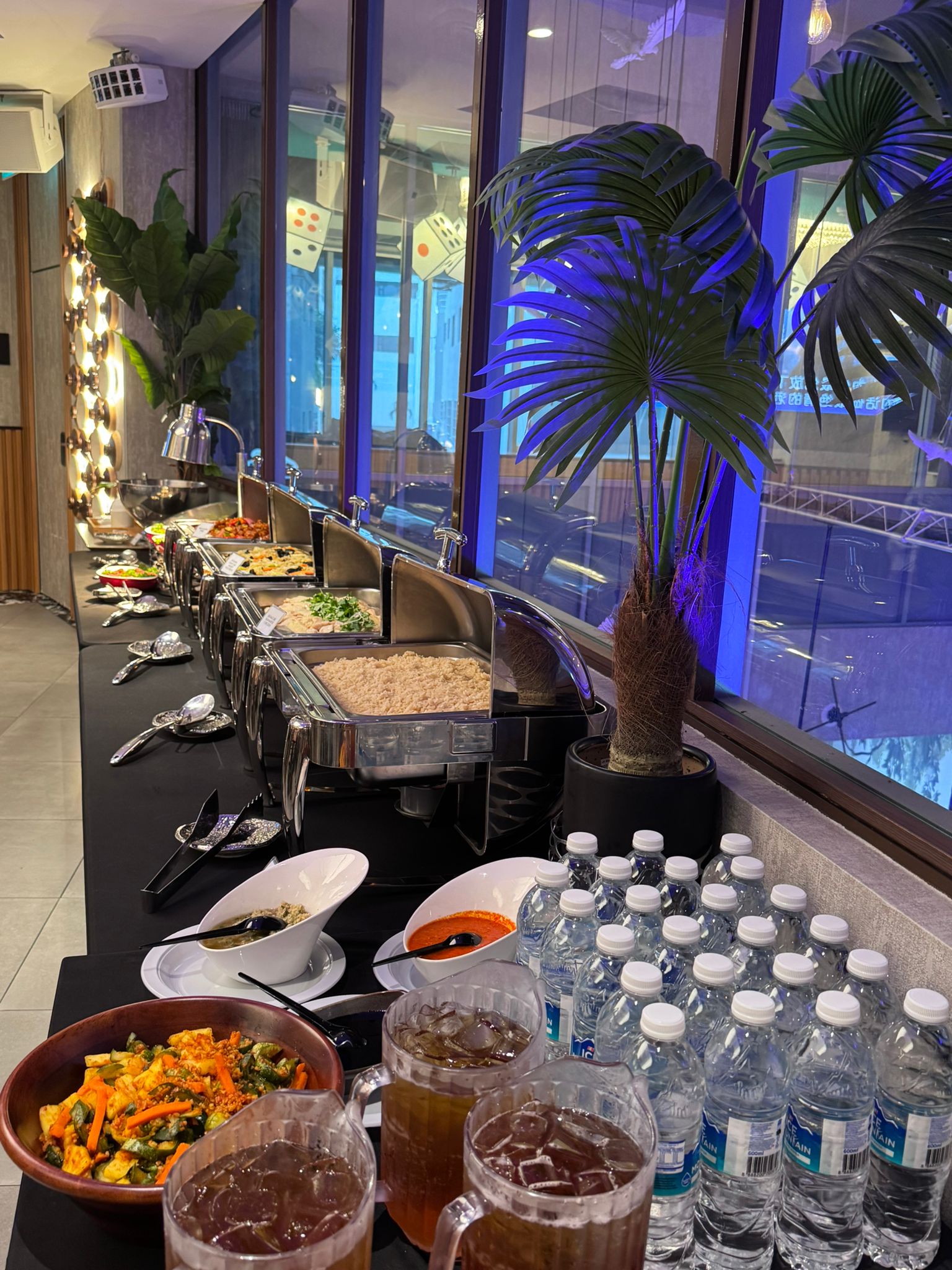 Buffet setup with food and water bottles near a window with blue lighting