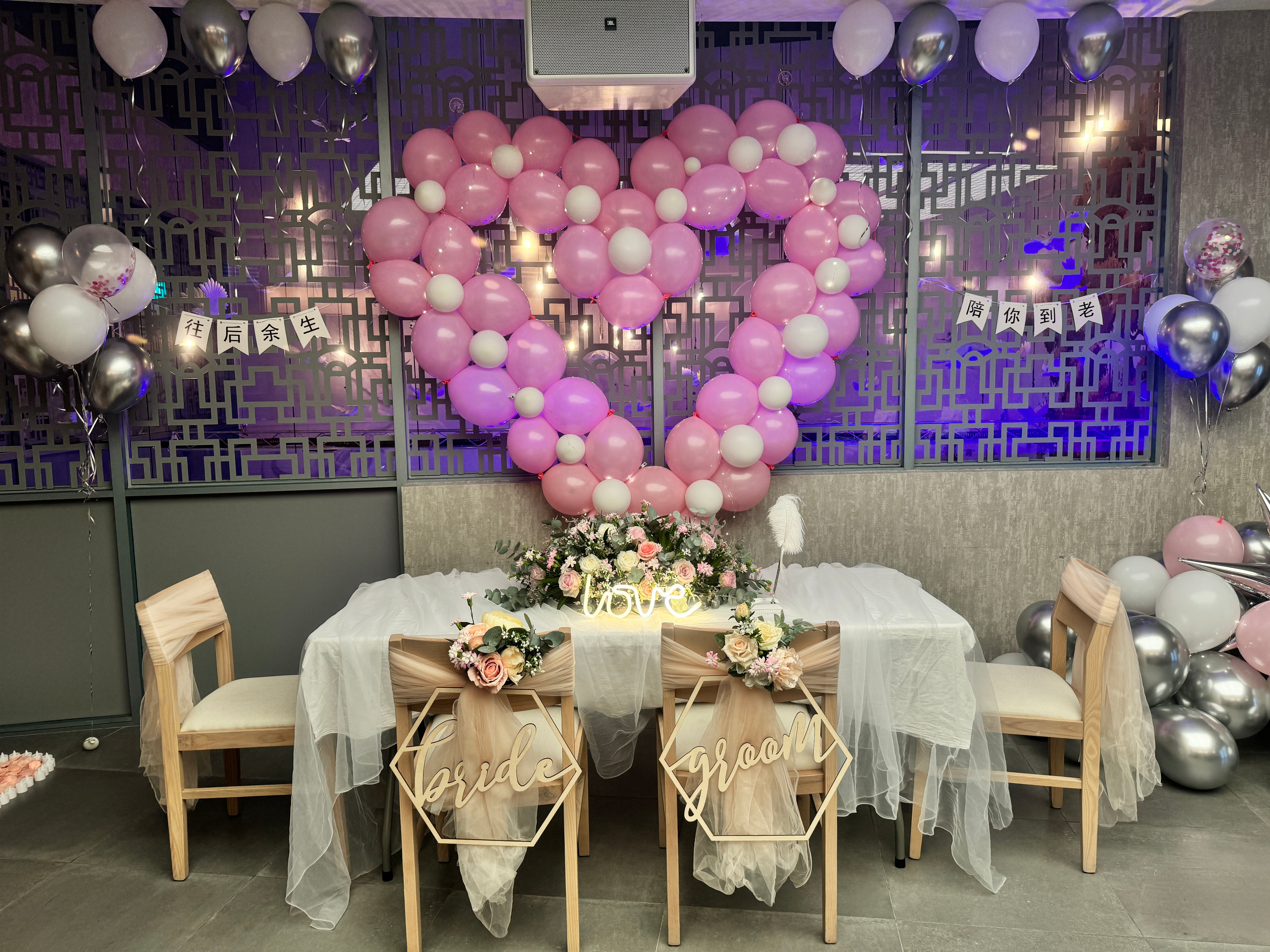 Decorated room with balloons, table settings, and floral arrangements for a celebration.