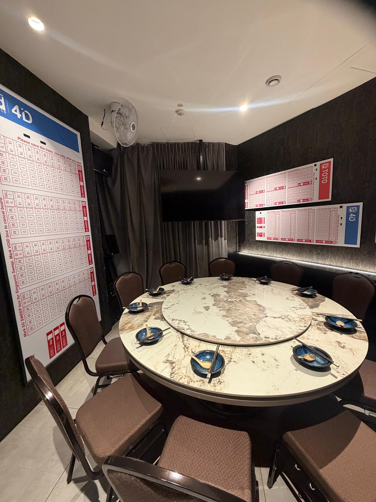 Dining area with a round table and chairs in a room with large screens and calendars on the walls in Clarke Quay.