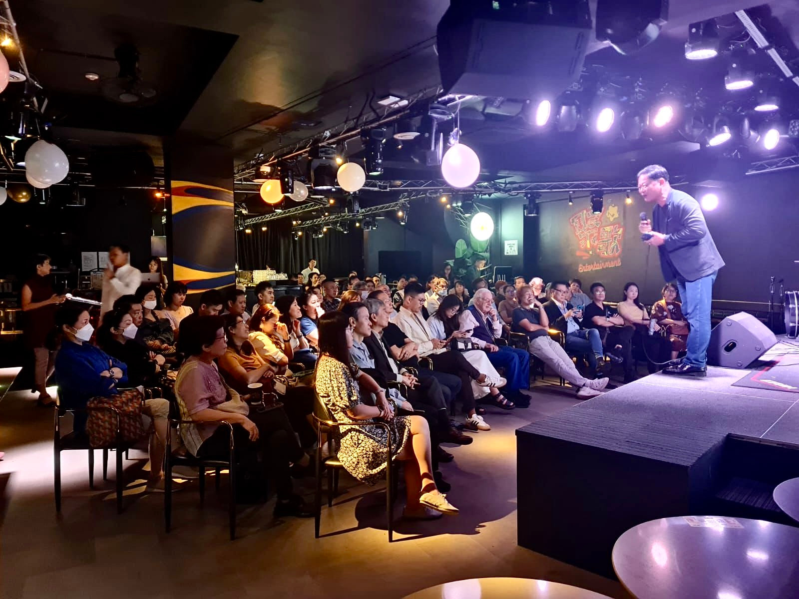 Person on stage addressing an audience in a live band setting