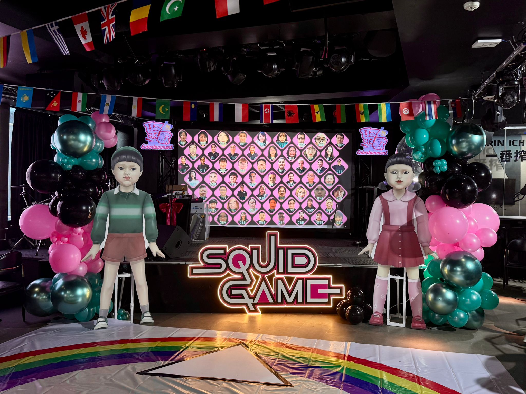 Decorated stage with 'Squid Game' theme, including props and colorful balloons.