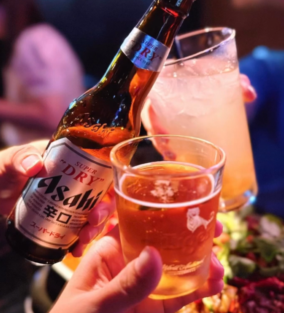 Person holding a bottle and two glasses of Asahi Super Dry beer.