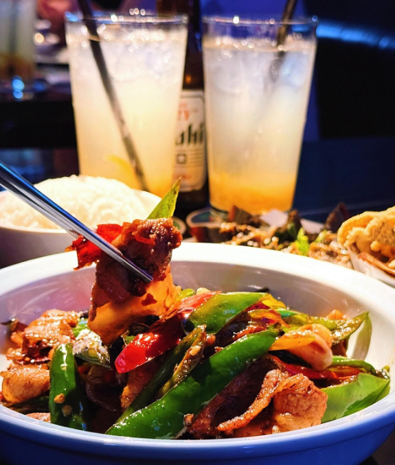Bowl of stir-fry with vegetables and meat, accompanied by two glasses of iced tea and a bottle of beer in Clarke Quay.