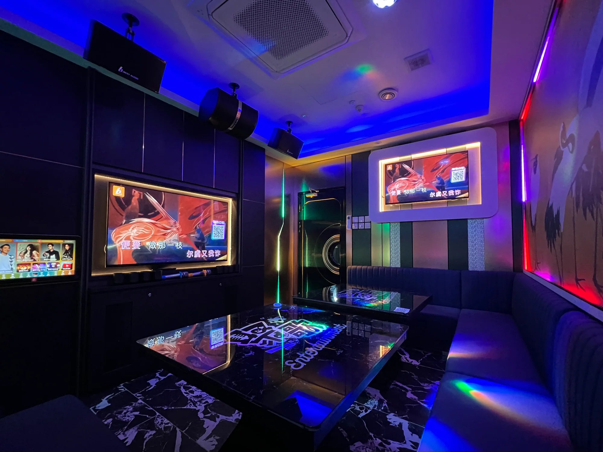 Modern karaoke room with multiple screens displaying colorful graphics, dim lighting, and a cozy atmosphere in Clarke Quay.