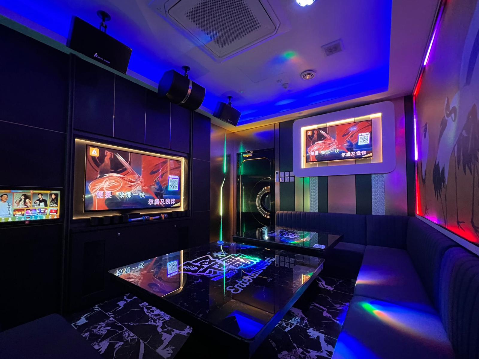 Modern karaoke room with multiple screens, a table, and colorful lighting in Clarke Quay.