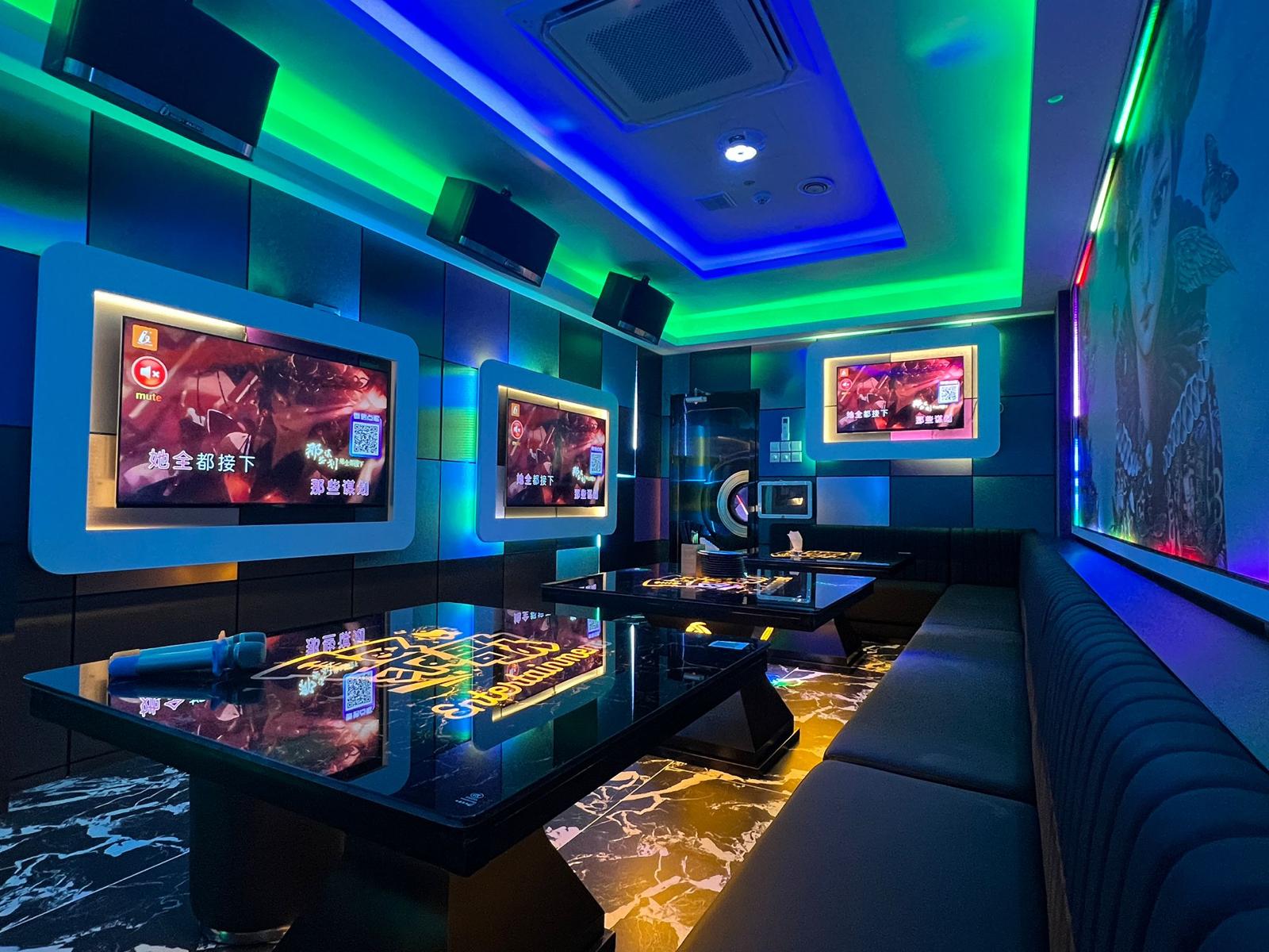 Modern karaoke room with colorful lighting, multiple screens displaying videos, and a cozy booth setup in Clarke Quay.