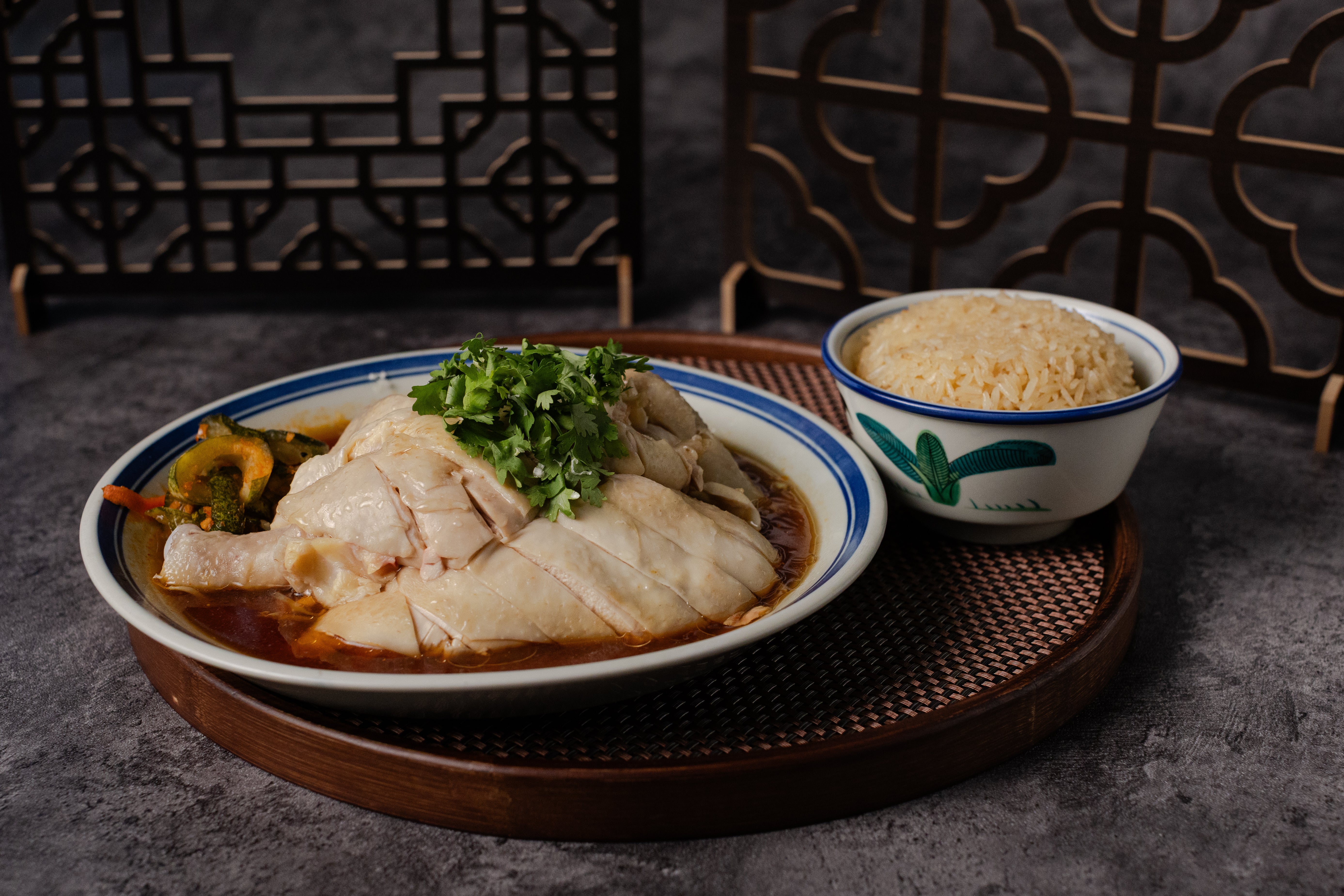 Plated dish of chicken rice with vegetables and a bowl of rice.
