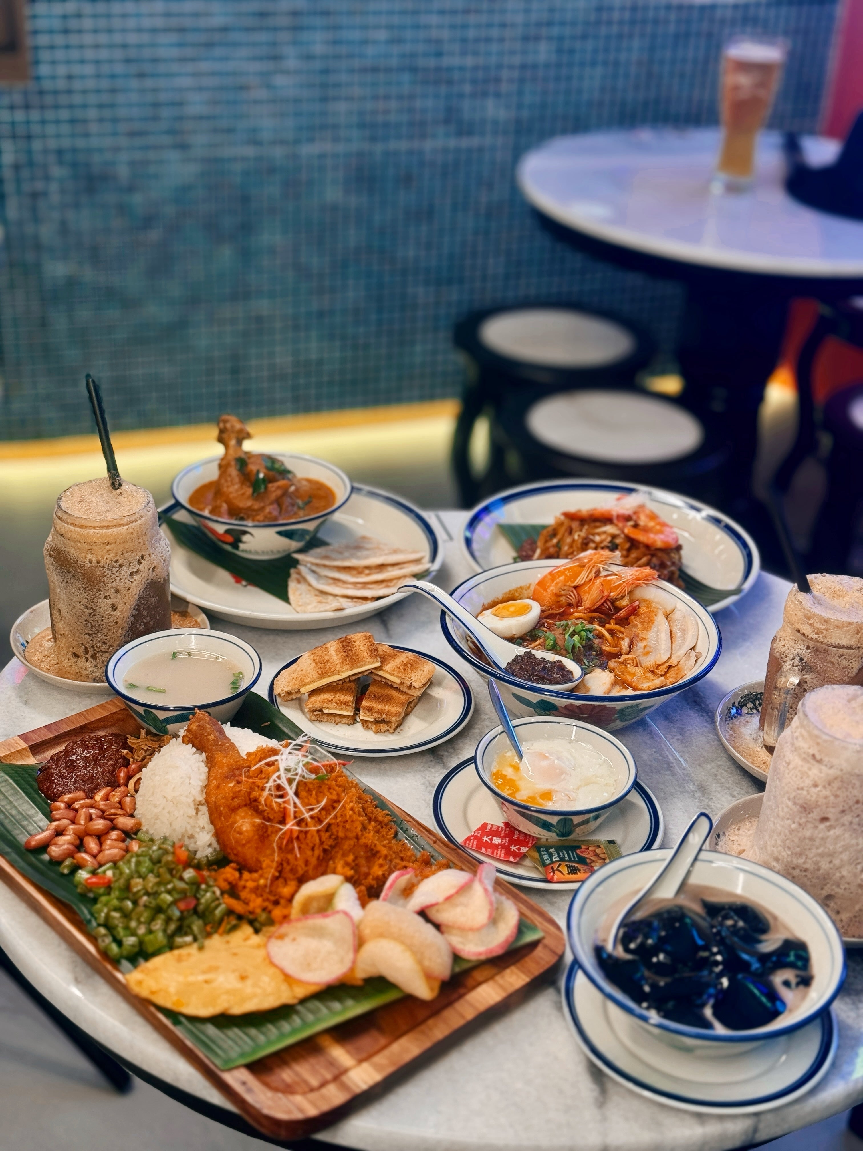 Assorted Nanyang dishes including drinks, noodles, and rice on a table.