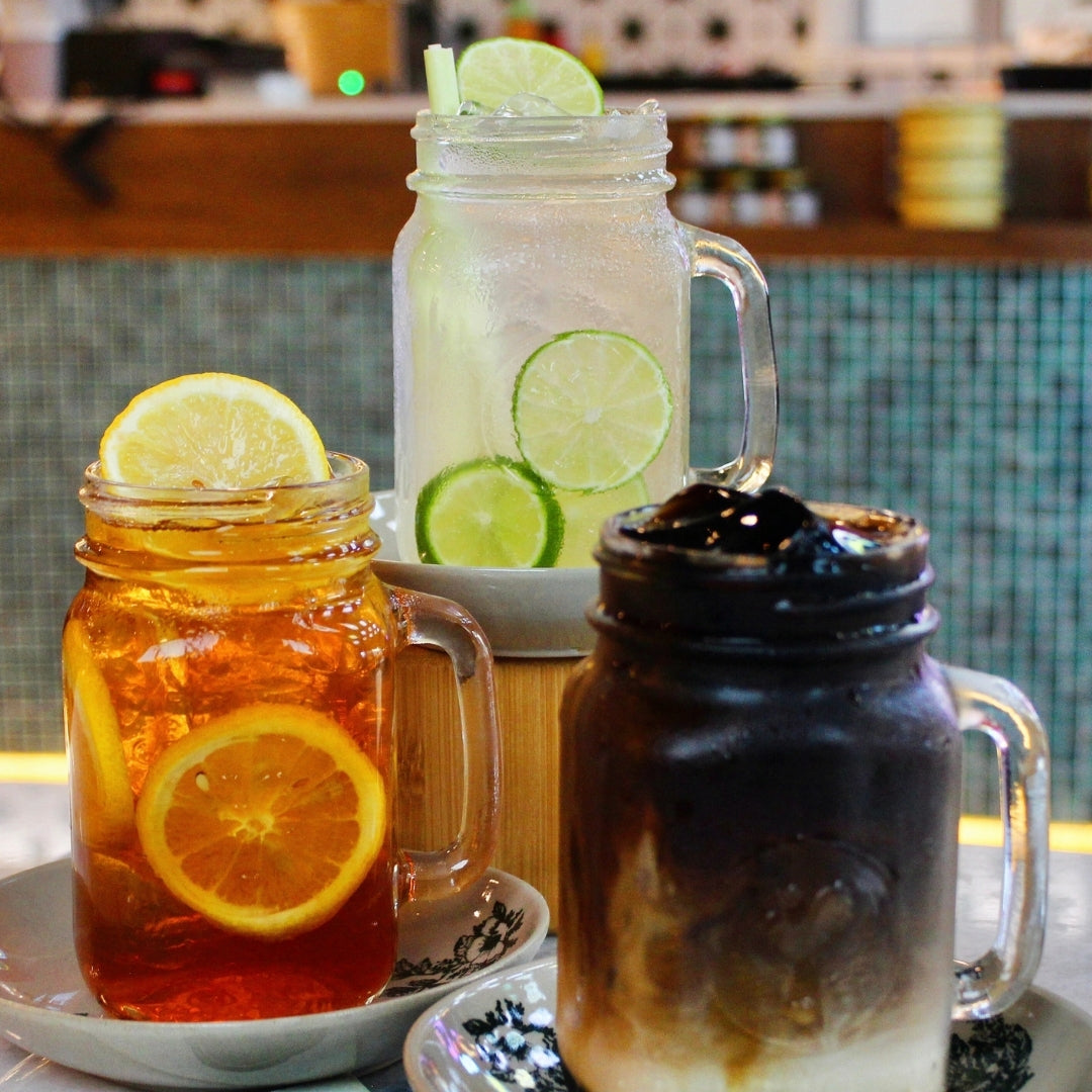 Three mason jars with different beverages on a table, including iced tea, lemonade, and iced coffee.