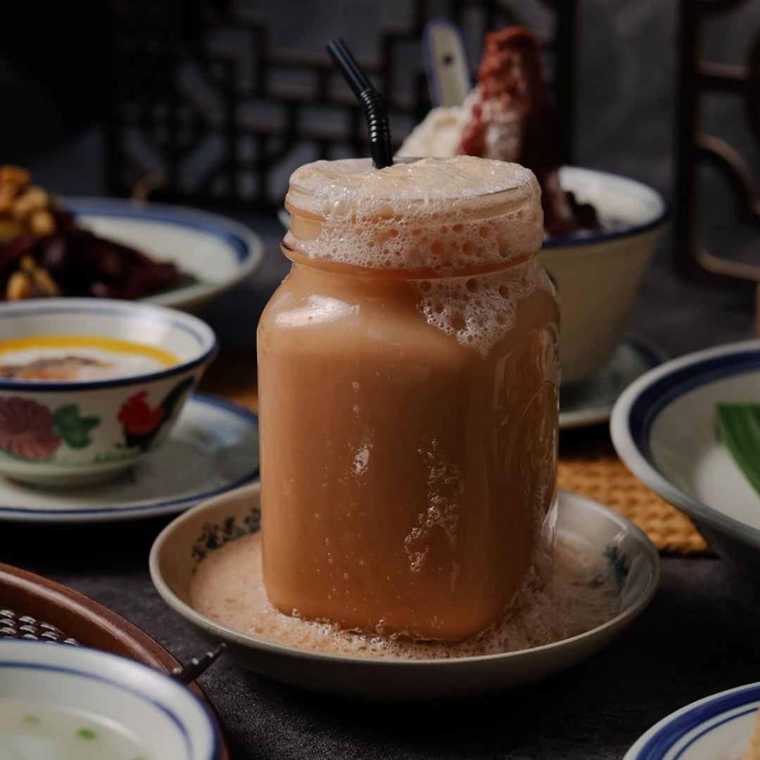 Mason jar filled with teh tarik on a table with various dishes in the background.